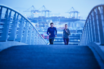 Runner couple running on urban footbridge at dawn