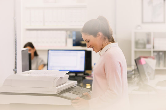 Smiling businesswoman making copies at copier in office