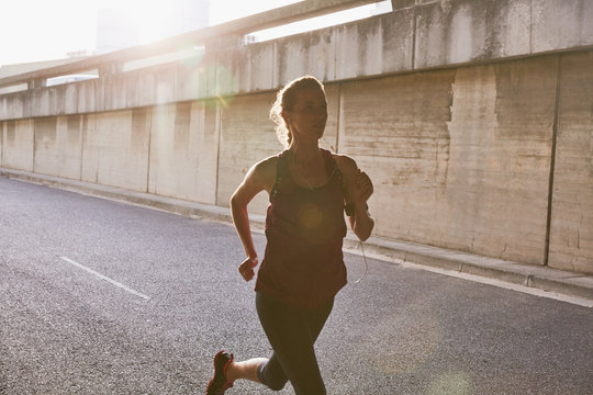 Silhouette female runner running on sunny urban street