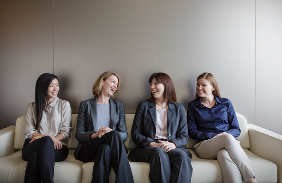 Smiling businesswomen talking in a row on sofa
