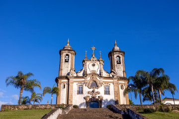 Fototapeta na wymiar Our Lady of Carmo church in historic colonial city centre of Ouro Preto with palm trees to the side and stairway leading up to the exterior facade and entrance