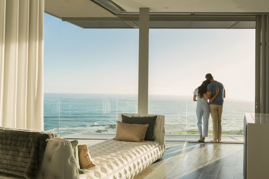 Affectionate couple hugging on sunny luxury balcony with ocean view