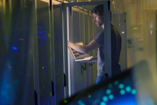 Server room technician with laptop at panel