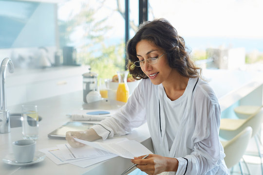 Businesswoman in bathrobe working reviewing paperwork at kitchen counter