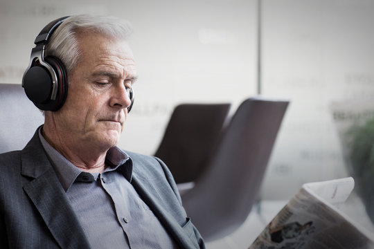 Senior businessman with headphones listening to music and reading newspaper