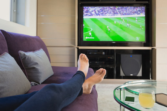 Personal perspective woman with bare feet up watching soccer game on TV in living room
