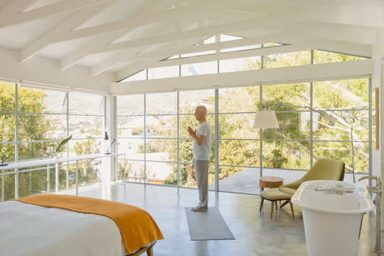 Mature man practicing yoga with hands at heart center in modern bedroom with vaulted wood beam ceilings