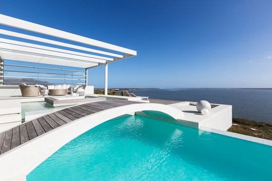 Sunny tranquil home showcase exterior infinity pool with ocean view under blue sky