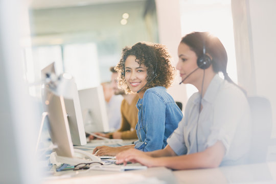 Portrait smiling businesswoman with headset working at computer in office