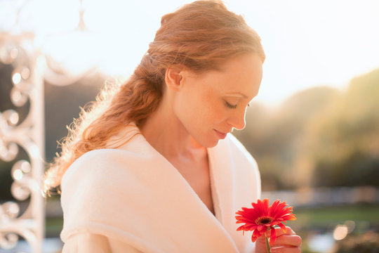 Serene woman holding red gerbera daisy on sunny patio