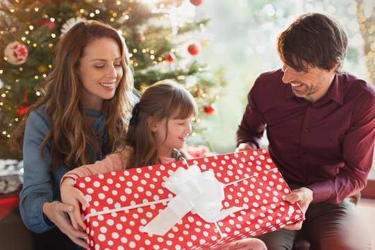 Parents giving large Christmas gift to daughter in front of Christmas tree