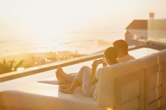 Silhouette couple using cell phone on chaise lounge with sunset ocean view