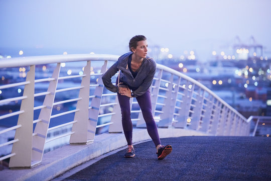 Female runner stretching leg on urban footbridge