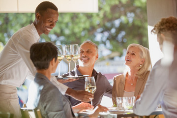 Waiter serving white wine to couples at restaurant table