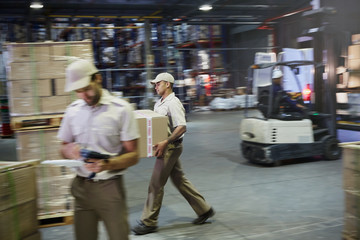 Workers carrying and moving boxes with forklift at distribution warehouse loading dock