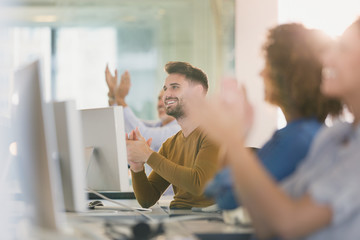 Business people at computers clapping in office