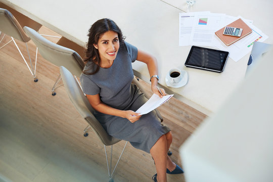 Portrait smiling businesswoman reviewing paperwork and drinking coffee at conference table