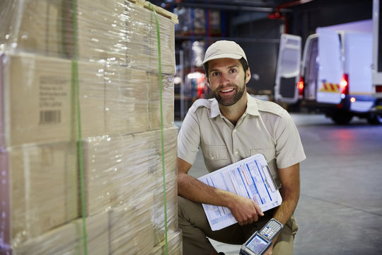 Portrait confident truck driver worker with scanner at pallet of cardboard boxes at distribution warehouse loading dock