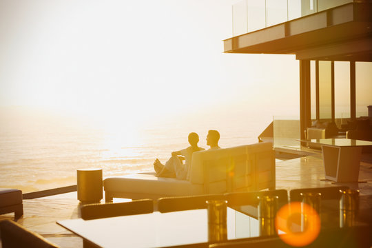 Silhouette couple relaxing on chaise lounge enjoying sunset ocean view