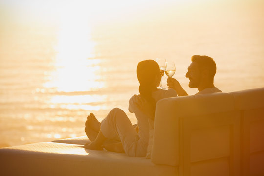 Silhouette couple toasting wine glasses on lounge chair with sunset ocean view