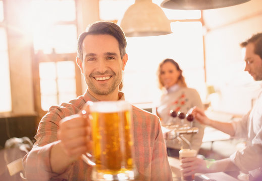 Portrait smiling man toasting beer stein in bar