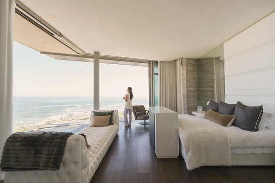 Woman looking at ocean view from modern luxury home showcase bedroom