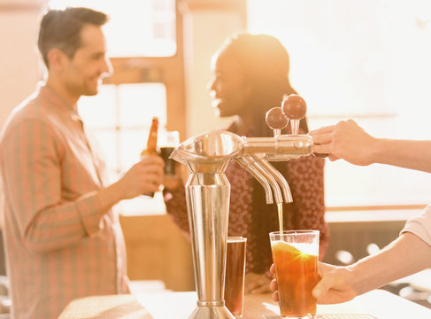 Couple drinking beer behind bartender pouring beer at beer tap in bar