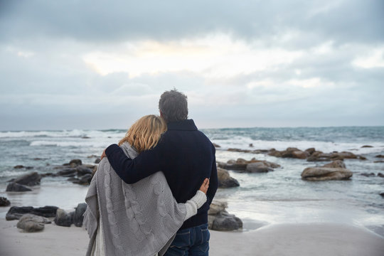 Serene affectionate couple hugging on winter beach looking at ocean