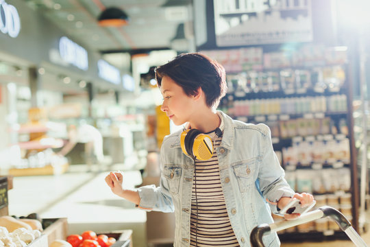 Young woman with headphones browsing, grocery shopping in market