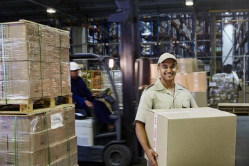 Portrait smiling worker carrying cardboard box at distribution warehouse loading dock