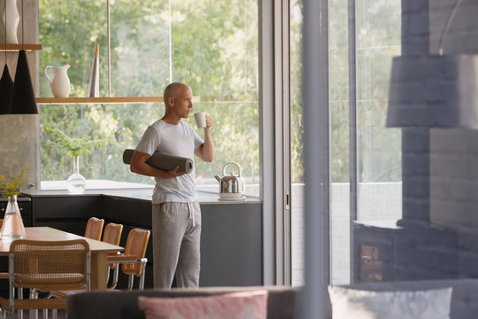 Mature man with yoga mat drinking coffee in kitchen