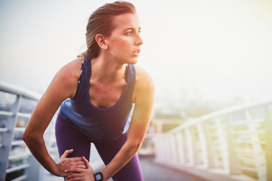 Female runner stretching leg on urban footbridge