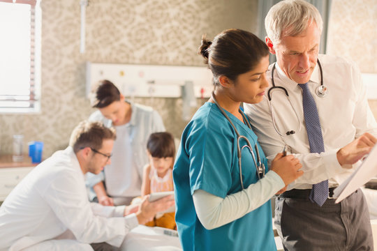 Male Doctor And Female Nurse Making Rounds, Reviewing Medical Record In Hospital Room