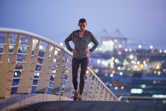 Female runner resting stretching legs on urban footbridge at dawn
