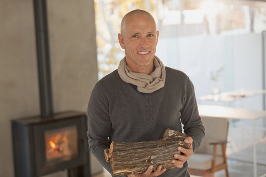 Portrait smiling mature man holding firewood in front of wood burning fireplace