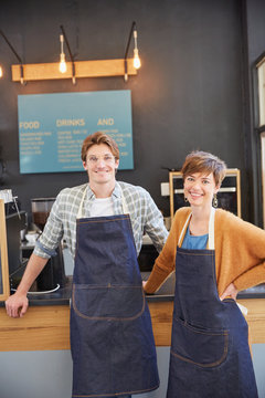 Portrait smiling cafe owners wearing denim aprons in cafe
