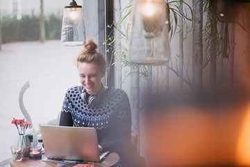 Smiling young woman using laptop in cafe window
