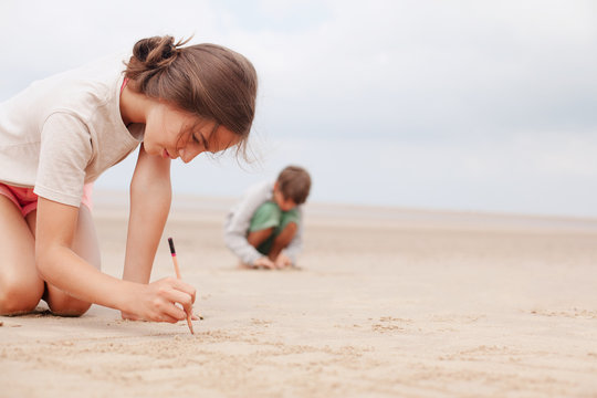 Girl with stick writing in sand on summer beach