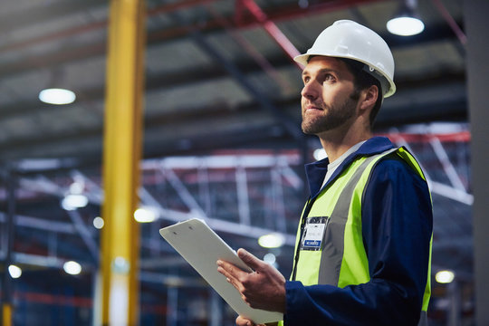 Worker with clipboard looking up in distribution warehouse