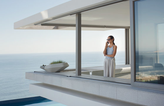 Woman talking on cell phone on modern, luxury home showcase exterior patio with ocean view