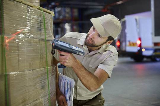 Truck driver worker with scanner scanning pallet of boxes in distribution warehouse