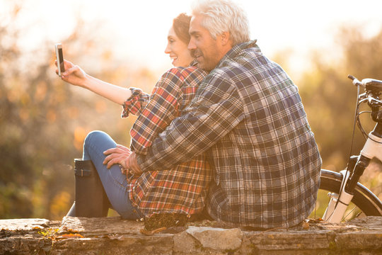 Affectionate couple hugging taking selfie with camera phone in autumn park