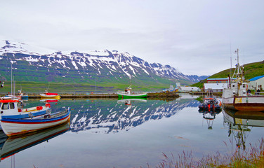 Colorful fishing boats and surrounding scenery landscape reflect in even surface of lake or bay in...