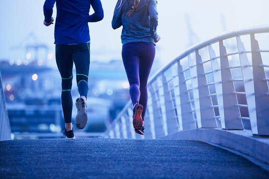 Runner couple running on urban footbridge at dawn