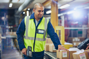 Worker with scanner scanning and processing boxes on conveyor belt in distribution warehouse