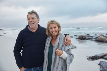 Portrait smiling senior couple hugging on stormy beach