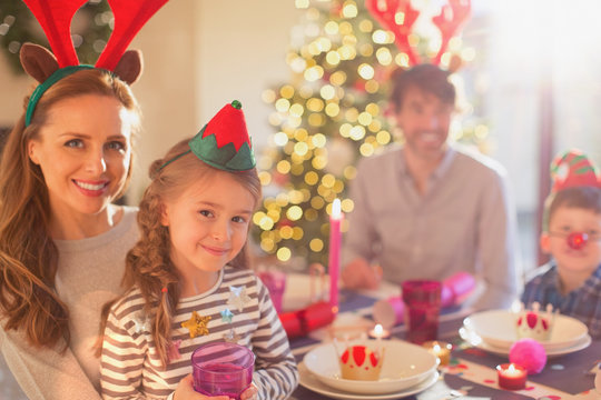 Portrait smiling mother and daughter wearing costume reindeer antlers at Christmas dinner table