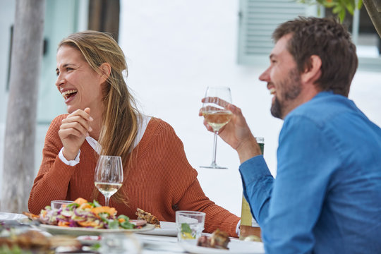 Laughing couple drinking white wine and eating lunch at patio table