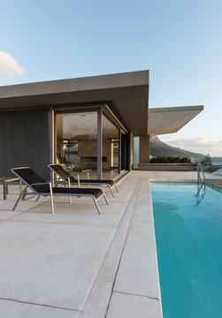 Lounge chairs along lap swimming pool outside modern luxury home showcase exterior