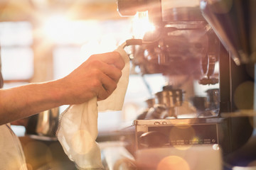Close up barista wiping down espresso machine milk frother with rag in cafe